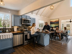 A modern kitchen with a central island, stainless steel appliances, and a dining area with a view. - Serene River Retreat | Double Decks, Hot Tub, Fire Pit & Scenic River Views (Shenandoah)