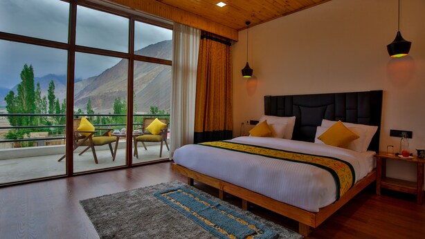 Une chambre avec un grand lit, une tête de lit en bois et une vue sur les montagnes grâce à de grandes fenêtres.