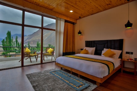 A bedroom with a large bed, wooden headboard, and a view of mountains through large windows.