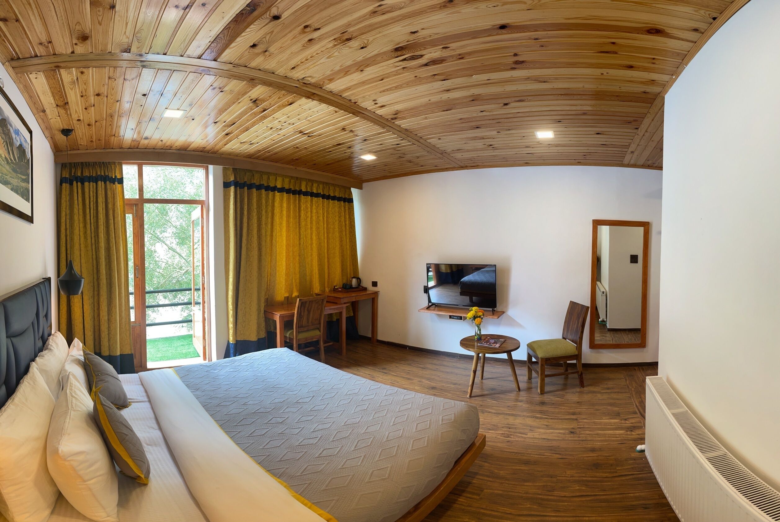 Habitación de hotel con una cama grande, un escritorio con silla, un televisor y una mesita de noche con un jarrón.