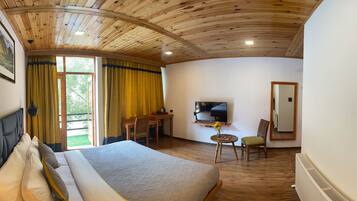 Habitación de hotel con una cama grande, un escritorio con silla, un televisor y una mesita de noche con un jarrón.