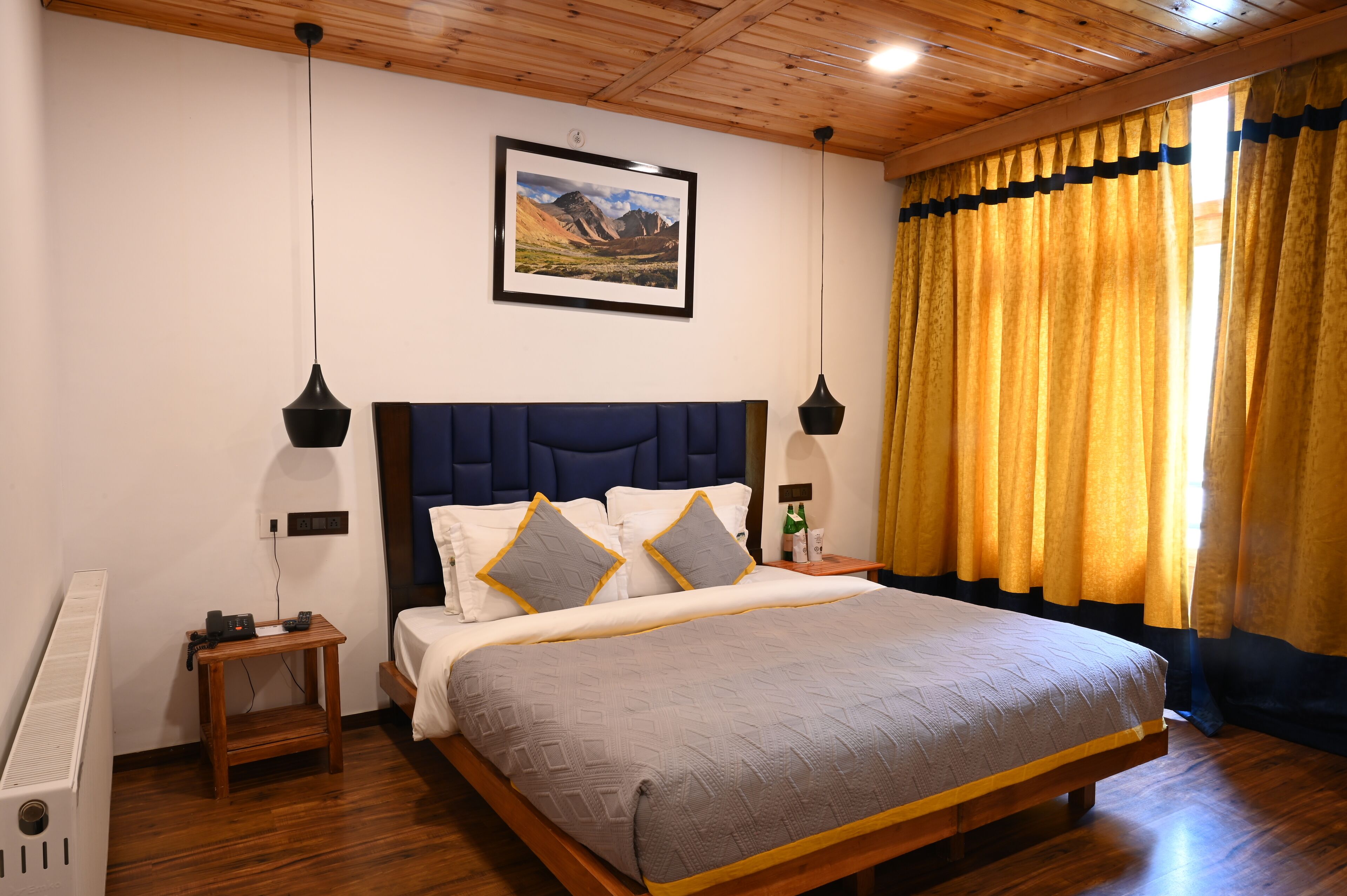 A bedroom with a large bed, wooden headboard, two bedside tables, a nightstand, a radiator, and a framed picture on the wall.
