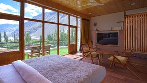 Une chambre avec un grand lit, des meubles en bois, une télévision et un balcon offrant une vue sur la montagne.