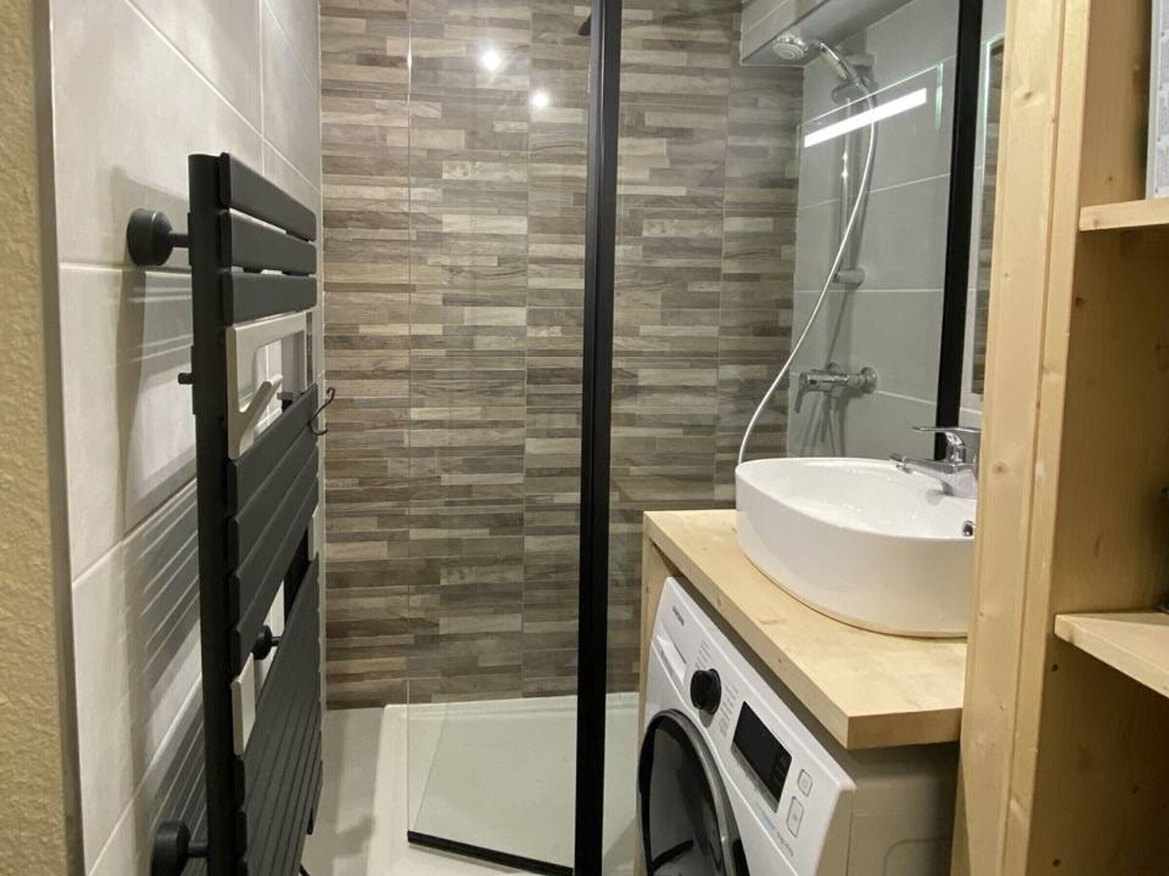 Een moderne badkamer met een glazen douchecabine, een inbouw wastafel en een wasmachine.