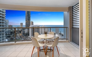 Un balcon avec une table ronde et des chaises, offrant une vue sur la ville, avec ses gratte-ciel et un ciel dégagé.