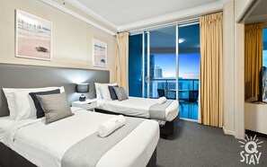 Une chambre d’hôtel avec deux lits, une table de chevet, une lampe et une vue sur le paysage urbain grâce à de grandes fenêtres.