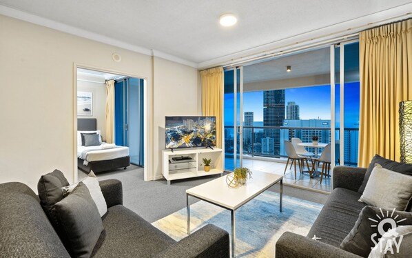 Une chambre d’hôtel moderne dotée d’un balcon, d’un lit, d’une télévision et d’un coin repas avec des chaises.