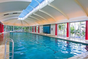 Une piscine intérieure dotée d’un plafond incurvé, de grandes fenêtres et de piliers rouges.