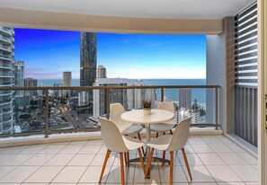 Un balcon avec une table ronde et des chaises, offrant une vue sur la ville, avec ses gratte-ciel et un ciel dégagé.