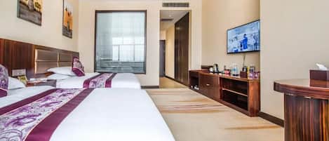 A hotel room with three beds, a TV, a desk, and a large window.