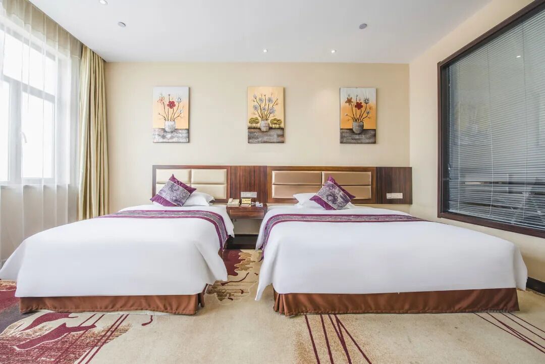 Habitación de hotel con dos camas, un ventanal grande y obras de arte en la pared.