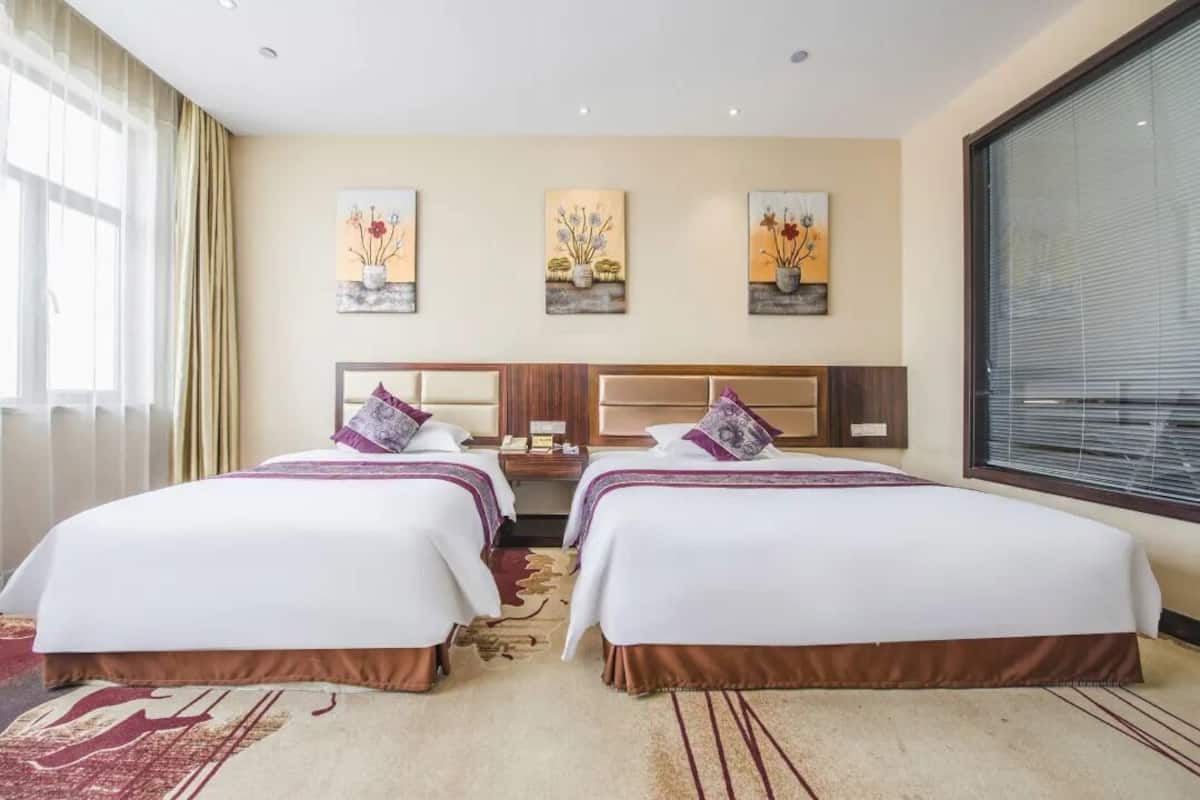 A hotel room with two beds, a large window, and artwork on the wall.