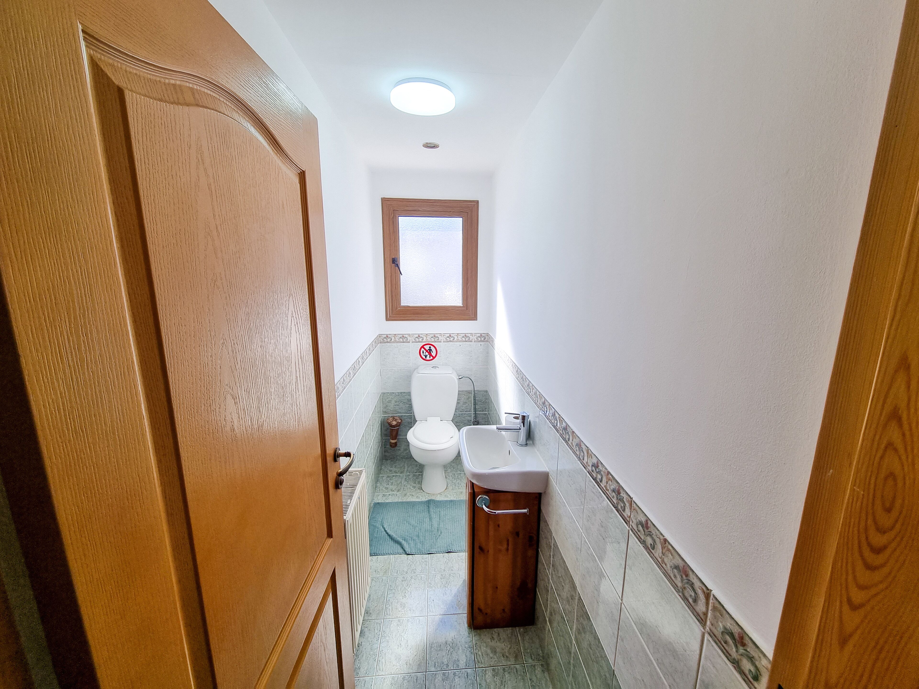 A narrow bathroom with a toilet, sink, and a small window.