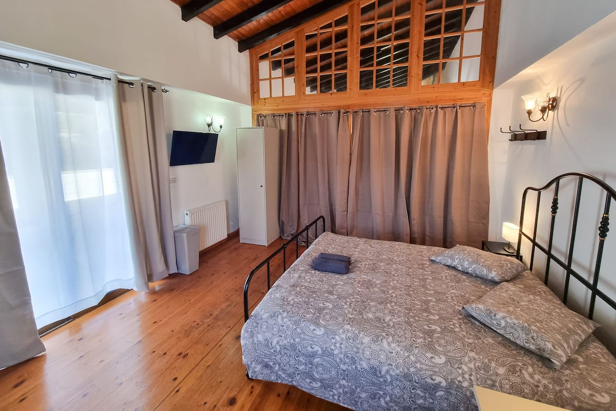 Ein Schlafzimmer mit Holzboden, einem Bett mit gemusterten Betttextilien, einem Heizkörper und einem an der Wand befestigten Fernseher.
