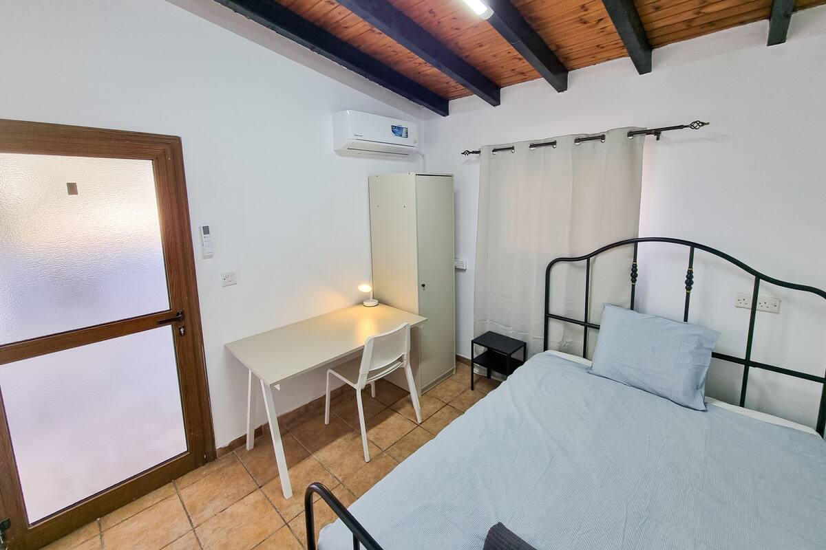 Ein Schlafzimmer mit einem Bett, einem Schreibtisch, einem Stuhl, einem Kleiderschrank und einem Fenster mit Vorhängen.