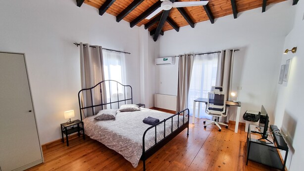 Une chambre avec un plancher en bois, un lit avec une tête de lit, un bureau avec une chaise et un ventilateur de plafond.