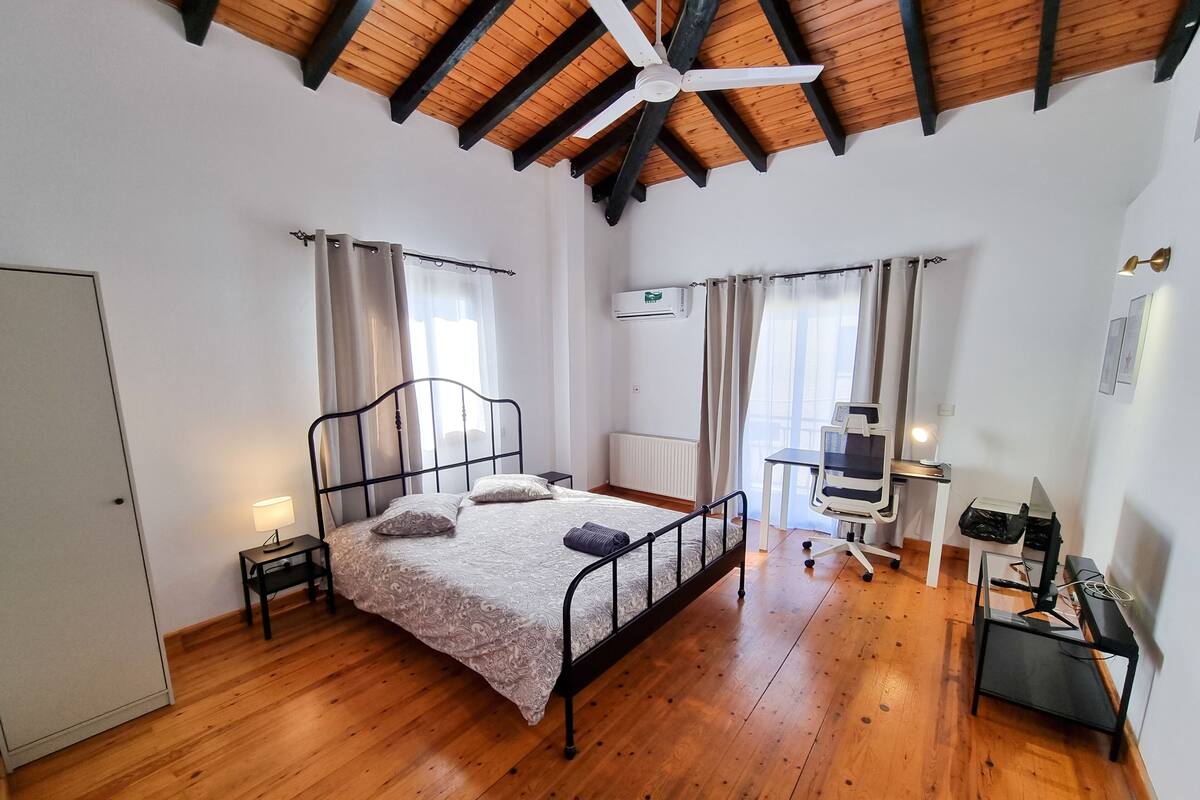 Ein Schlafzimmer mit Holzboden, einem Bett mit Kopfteil, einem Schreibtisch mit Stuhl und einem Deckenventilator.