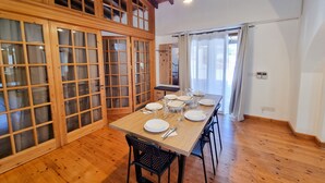 Un coin repas avec une table en bois dressée pour quatre personnes, entourée de chaises noires. Une porte en bois avec des panneaux de verre est visible sur la gauche.