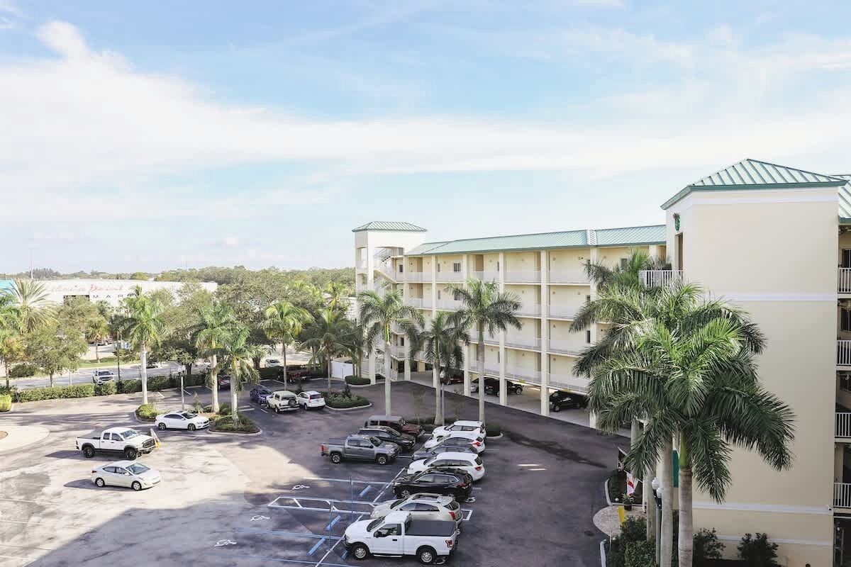 Un hotel con estacionamiento, varios pisos y palmeras.