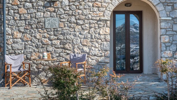 Un edificio de piedra con un amplio arco de entrada, una mesa pequeña con una silla, y una vista de montañas nevadas a través de la ventana.