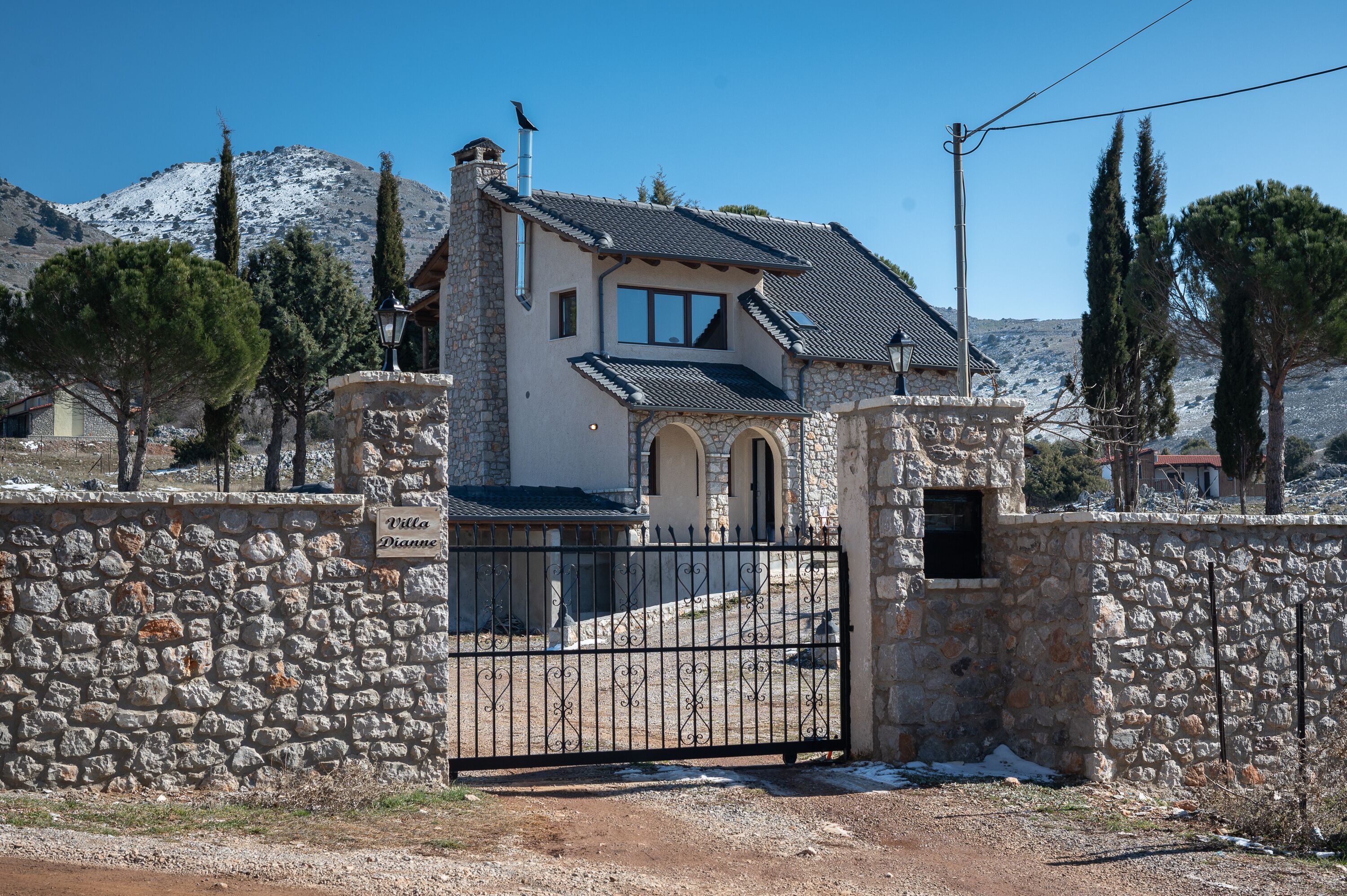 Una villa de paredes de piedra con techo de tejas, una puerta y montañas al fondo.