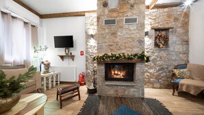 Una sala de estar acogedora con chimenea de piedra, un televisor montado en la pared y un espacio de descanso confortable con un banco y un sofá.