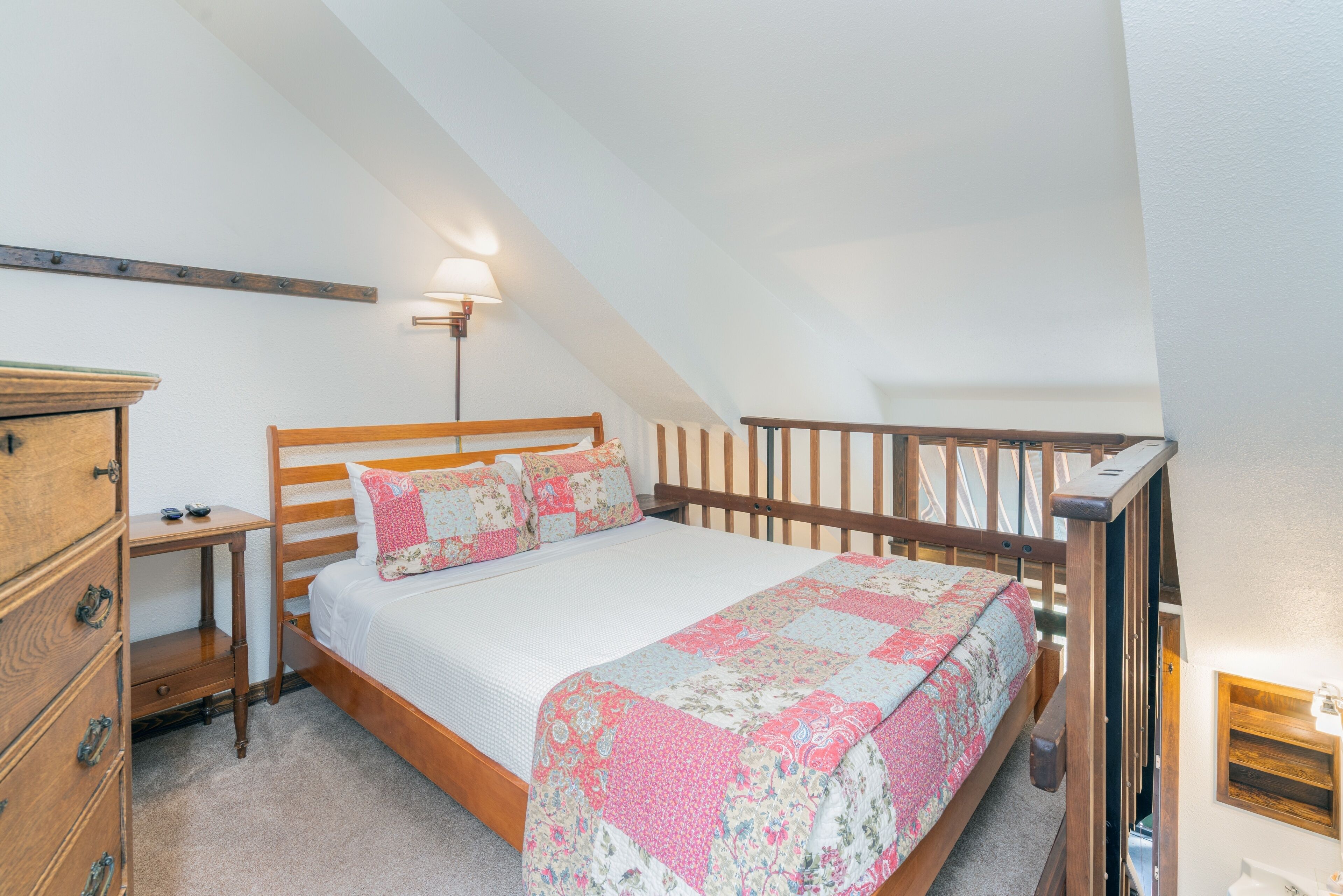 A bedroom with a wooden bed, a nightstand, a dresser, and a sloped ceiling.