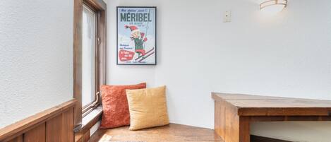 A corner with a wooden bench, a poster on the wall, and a window with a view.
