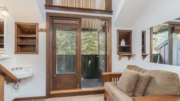 A room with a wooden bench, a sofa, a sink, and a glass door leading to a balcony.