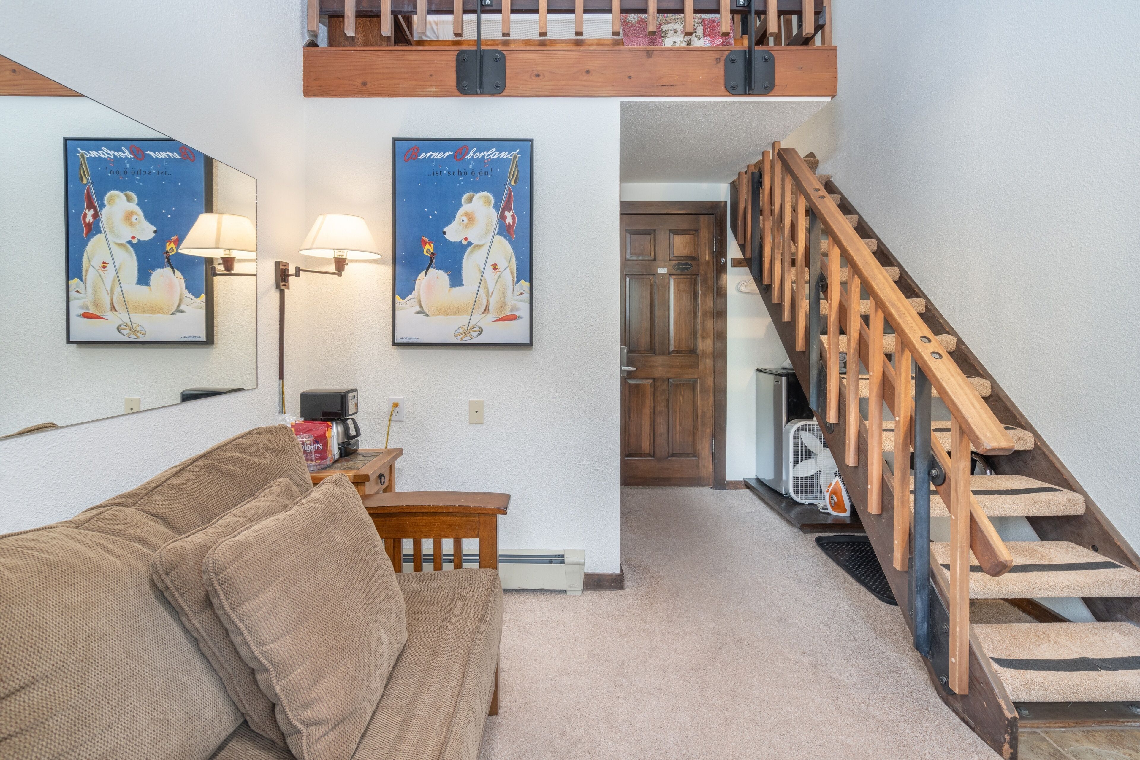 A living room with a sofa, two wall-mounted lamps, and a staircase.