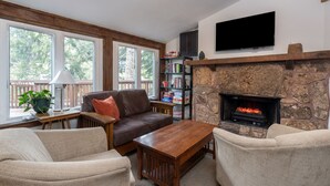 Una sala de estar con chimenea de piedra, un televisor montado encima y una estantería.