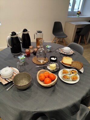 A breakfast table with coffee makers, a jug, a bowl of oranges, muffins, toast, and a cup of tea. - Maison 2 chambres d'hotes with large garden in quiet stone village. (Villemoirieu)