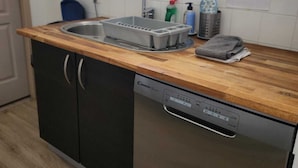 Une cuisine équipée d’un évier, d’un lave-vaisselle et d’une fenêtre donnant sur un espace verdoyant.