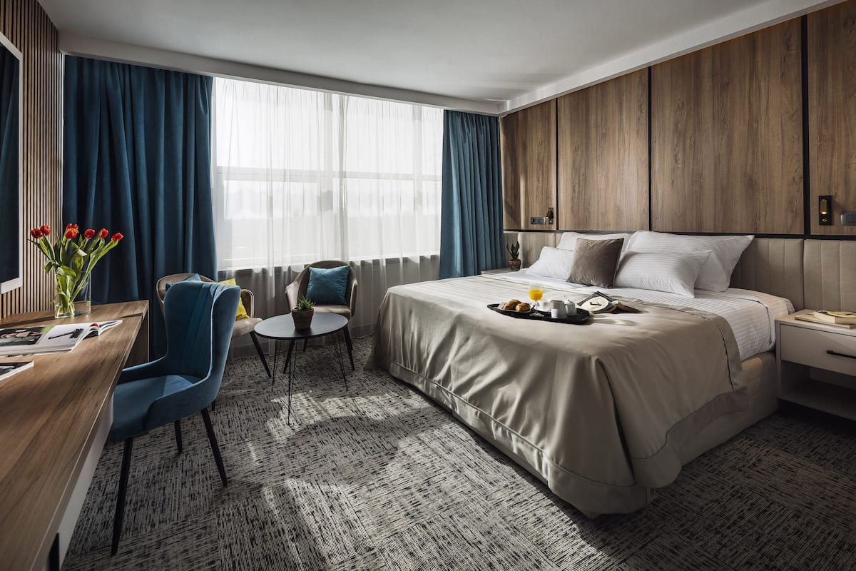 Een hotelkamer met een bed, een bureau met stoel, een klein tafeltje met stoel, en een raam met gordijnen.