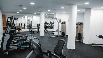 Une salle de sport équipée de divers appareils d’exercice, notamment des tapis de course et des appareils de musculation, disposés dans un espace vaste aux murs et aux colonnes blancs.