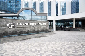 The Grand Hotel Zagreb's entrance with a stone wall and a modern building in the background.