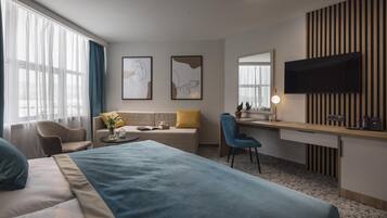 Una habitación de hotel con una cama, un sofá, un escritorio, una silla, un televisor y una ventana con cortinas.