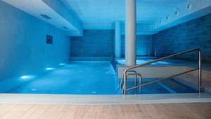An indoor swimming pool with a tiled floor, a metal handrail, and a tiled wall.