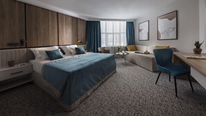 A modern hotel room with a large bed, a desk, a sofa, and a window with curtains.