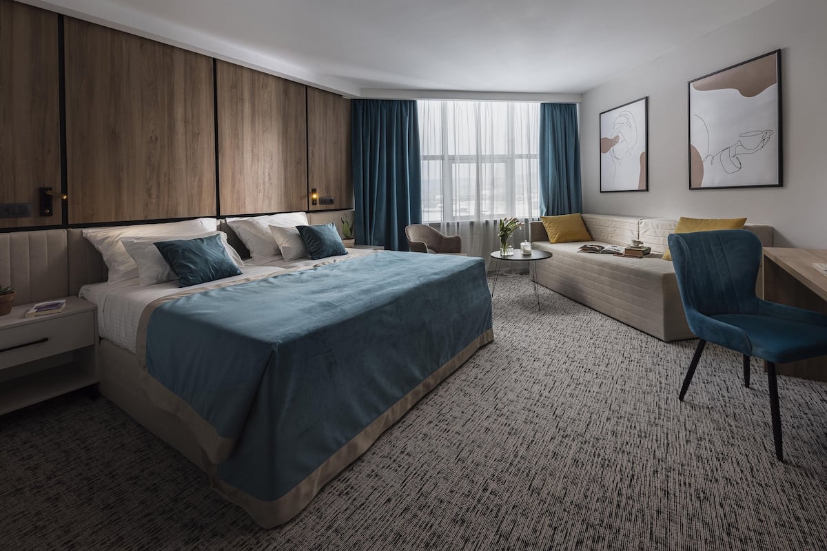 Een moderne hotelkamer met een groot bed, een bureau, een slaapbank en een raam met gordijnen.