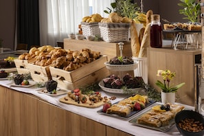 A buffet with various pastries, fruits, and a bottle of syrup.