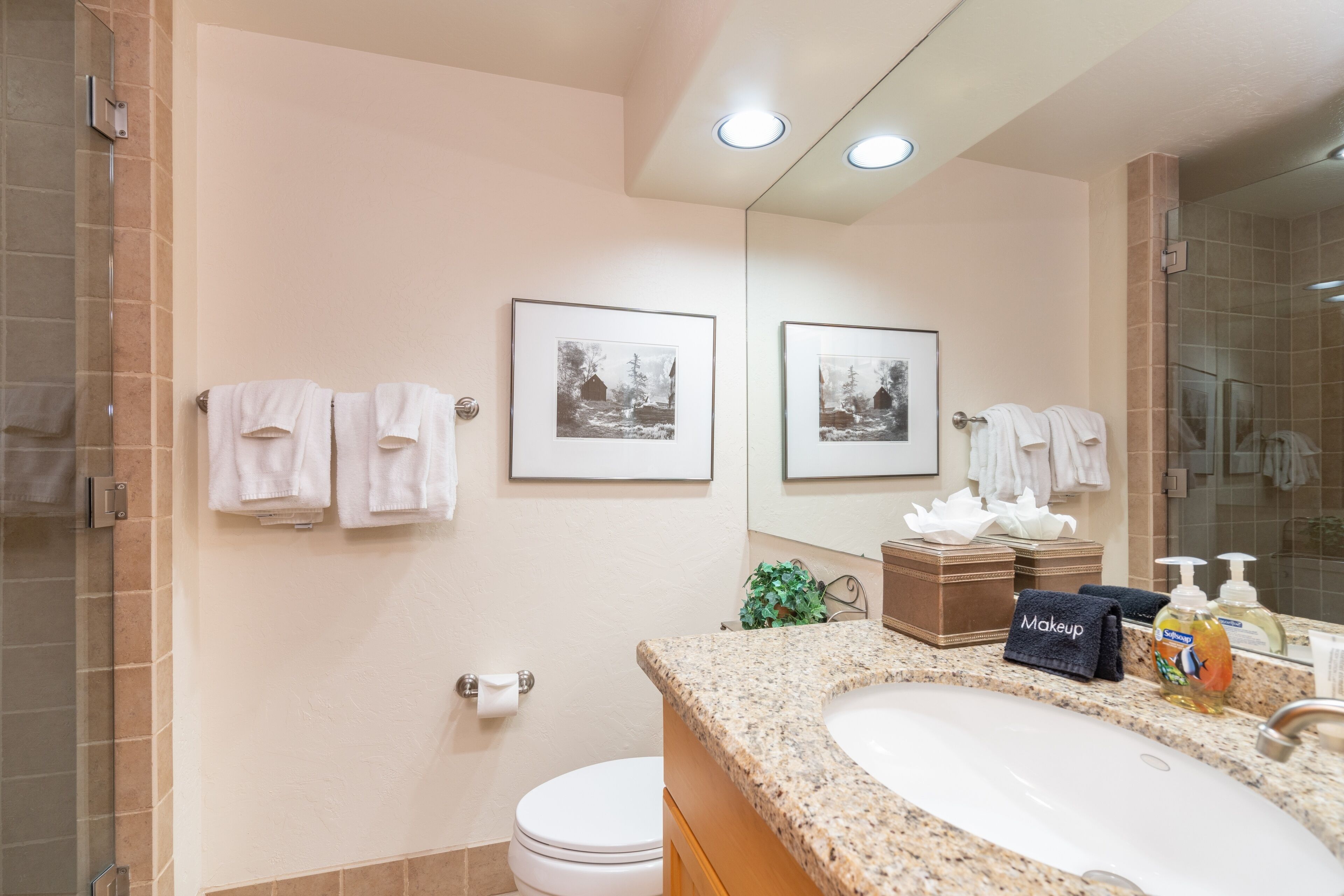 A bathroom with a granite sink, a mirror, a toilet, and framed pictures on the wall.