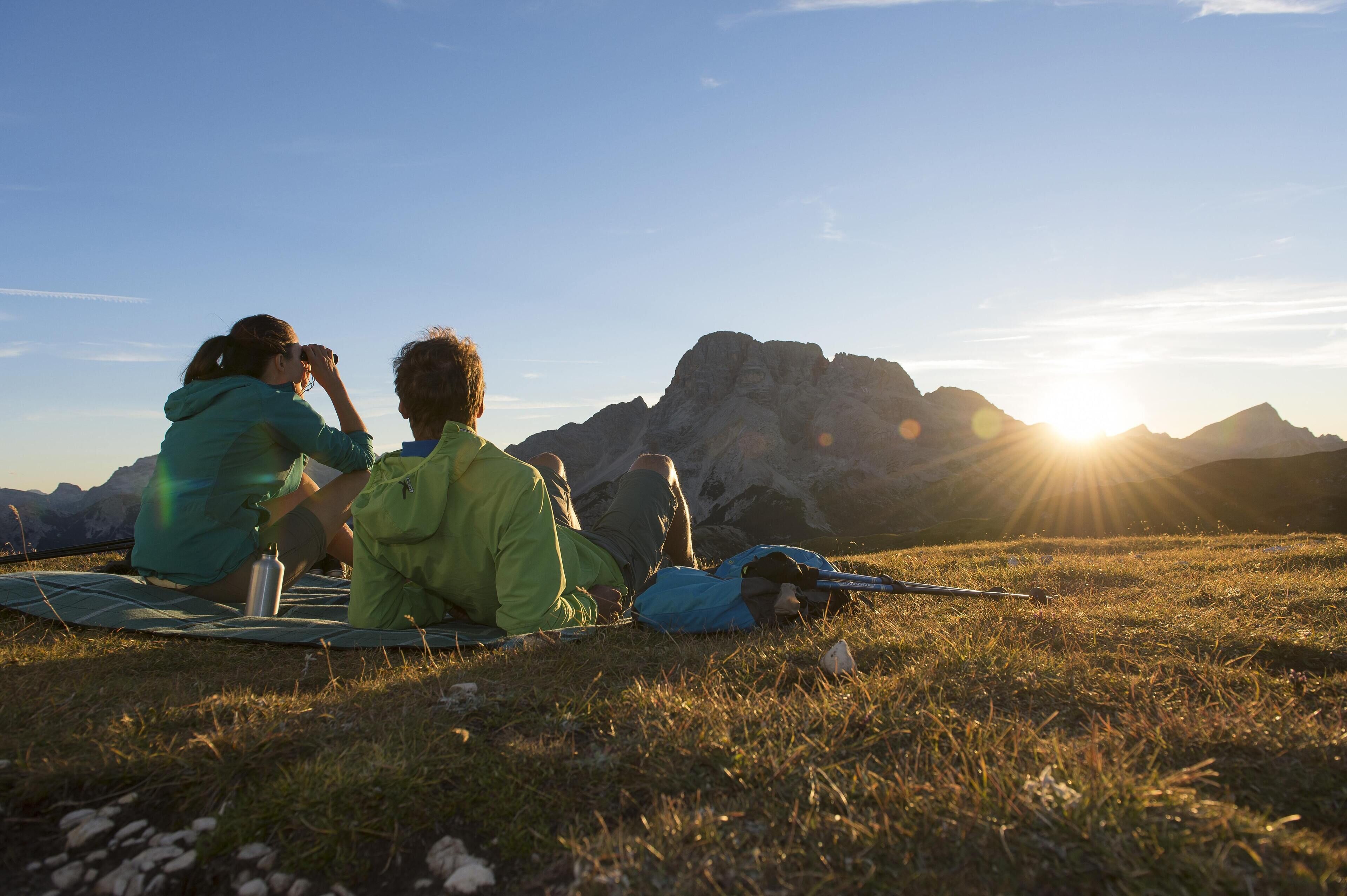 Two people sitting on a blanket outdoors with mountains in the background.