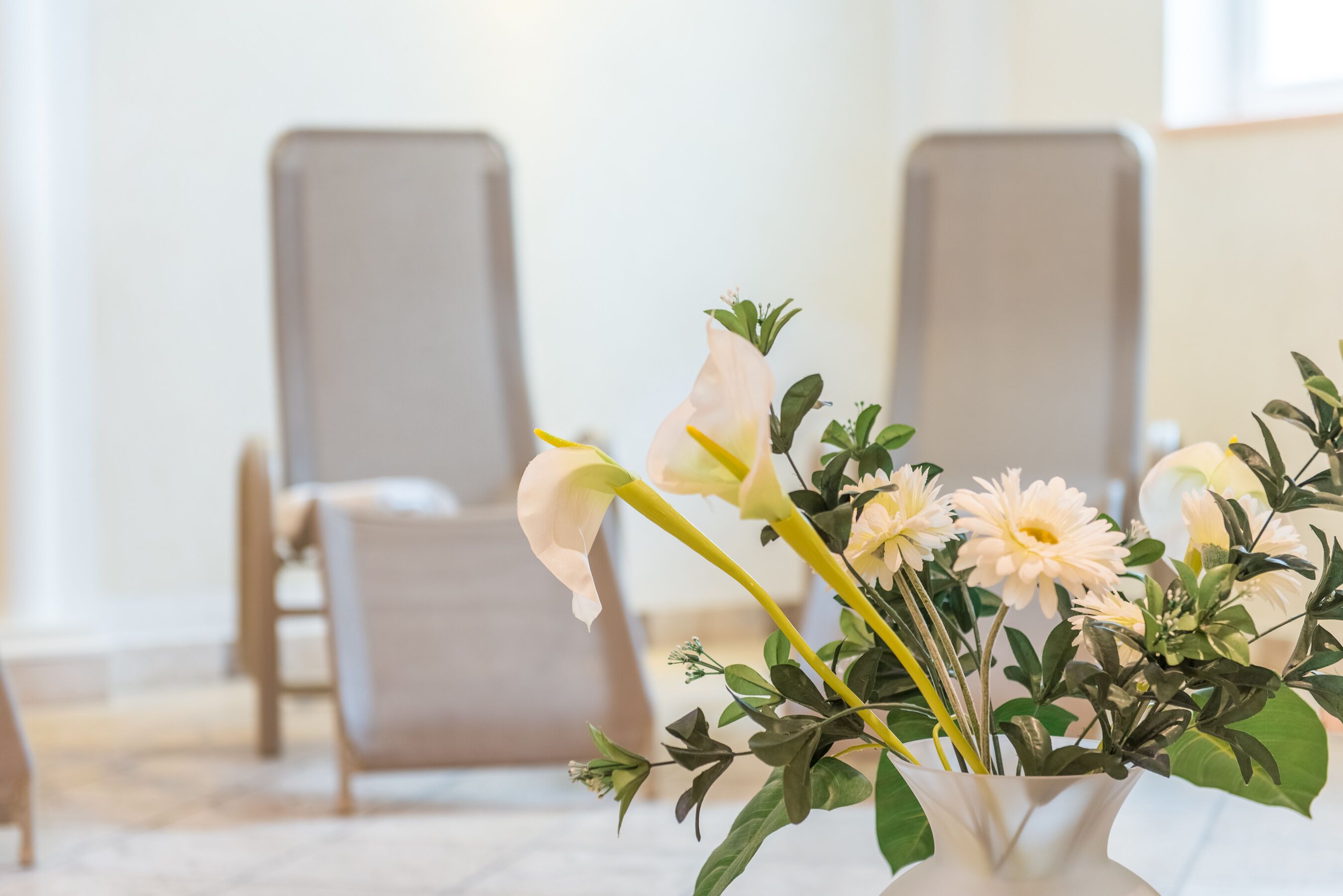 Eine weiße Vase mit Blumen auf einem Tisch in einem Raum mit zwei Stühlen.
