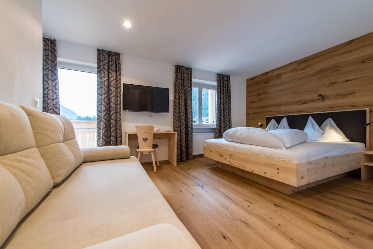 Et moderne hotelværelse med trægulv, en stor seng, en sofa, et skrivebord og et fjernsyn.