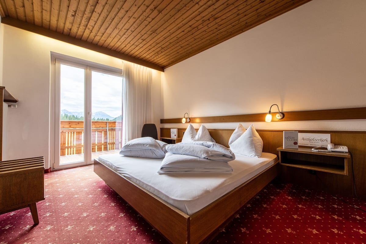 Et hotelværelse med træloft, en stor seng med hvide sengetøj, et natbord med en lampe, udsigt til bjerge gennem vinduet og et rødt tæppede gulv.