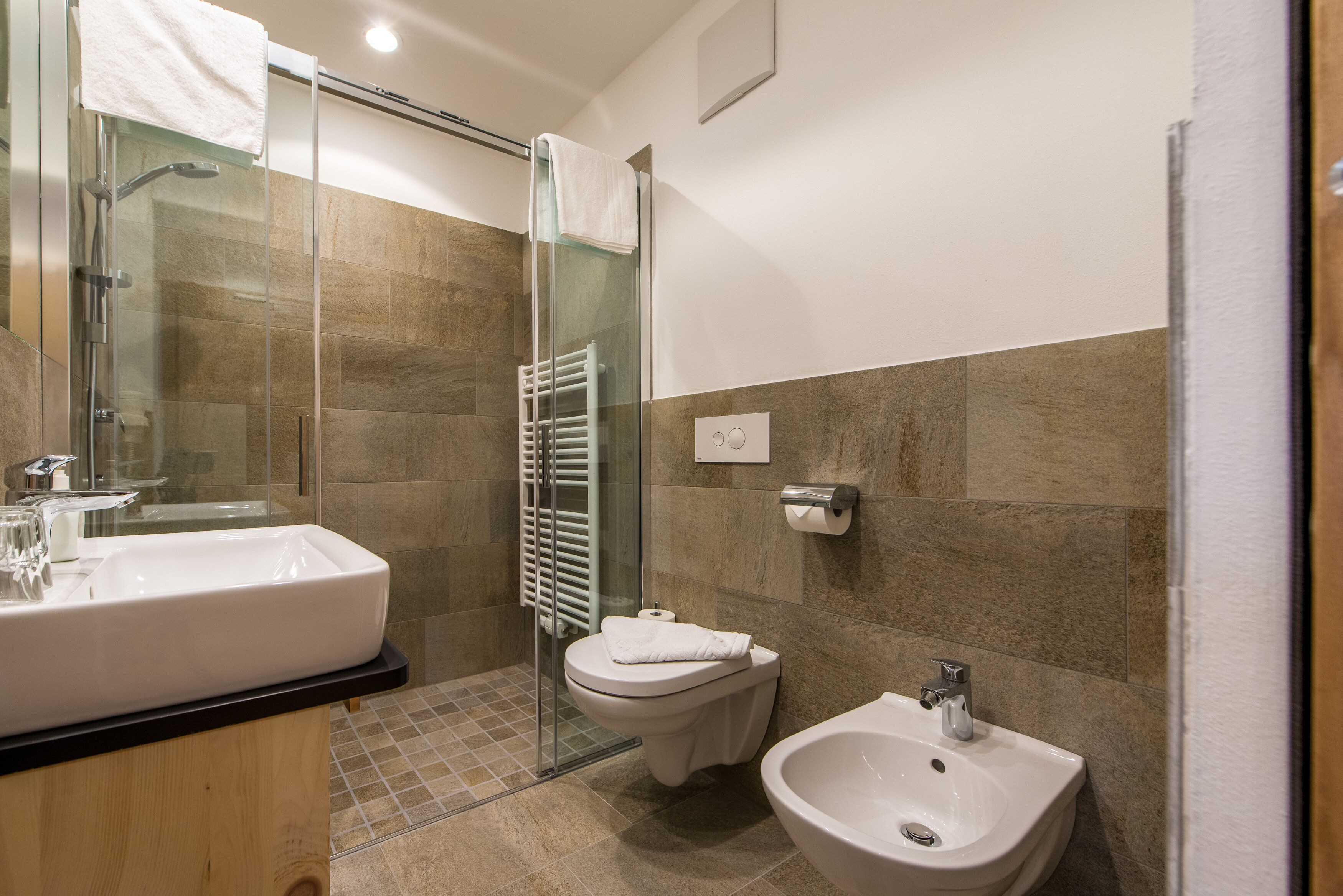 A modern bathroom with a glass shower enclosure, a white sink, a bidet, and a toilet.