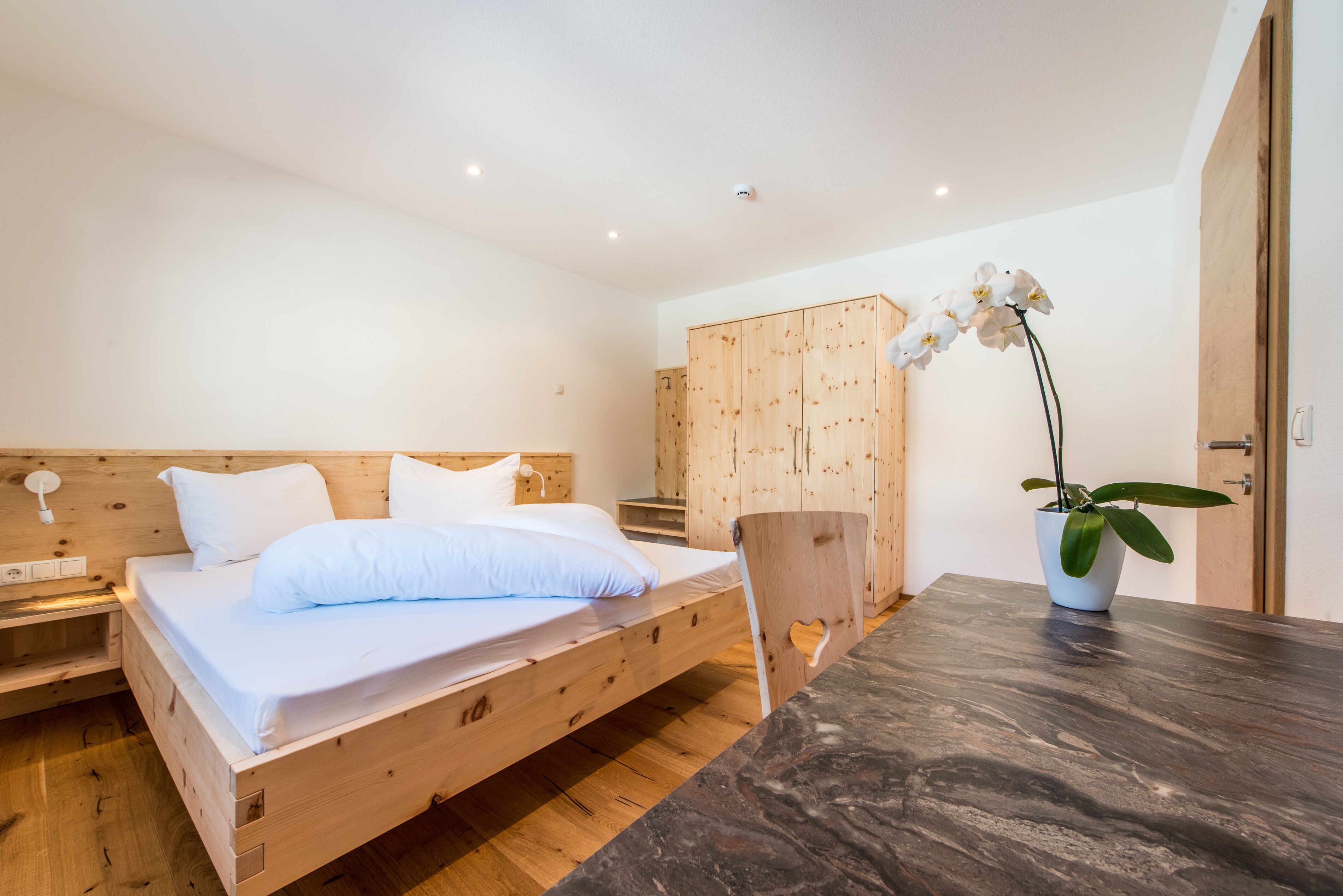 Un dormitorio con una cama de madera, una mesita de noche, un armario y una orquídea en maceta.