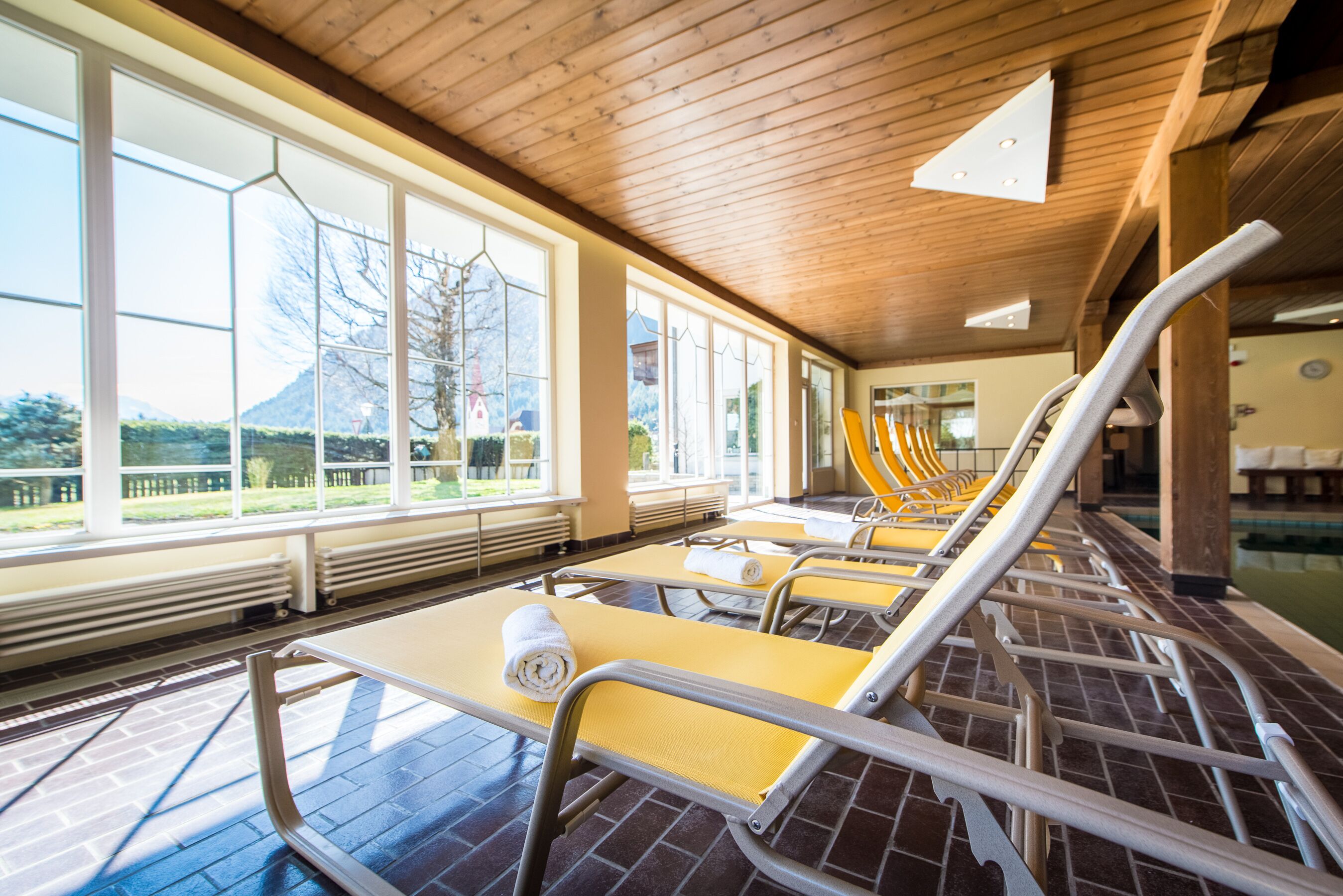 A row of sunbeds with towels, large windows, and a view of a mountain.