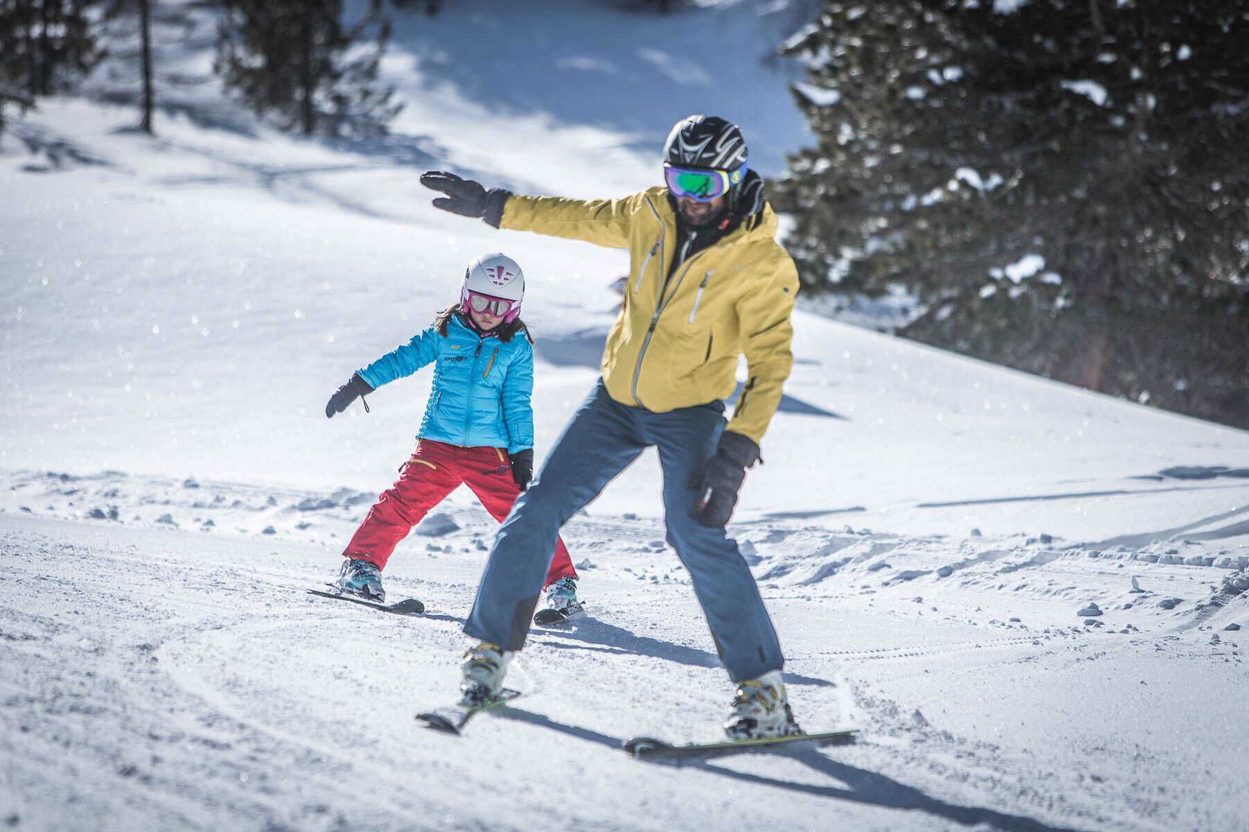 A snowy slope with a person skiing and a child in a blue jacket.